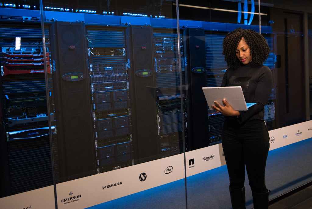 A woman looks at a laptop in front of a server rack